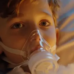 Chłopiec w masce inhalacyjnej leżący w łóżku.