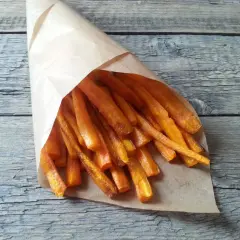 Chrupiące frytki z marchewki w papierowym rożku, ułożone na drewnianym blacie. Zdrowa przekąska.