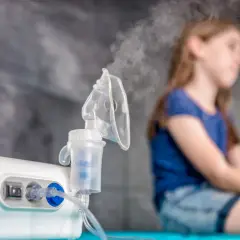 Inhalator z mgiełką i niewyraźna postać dziewczynki w tle.