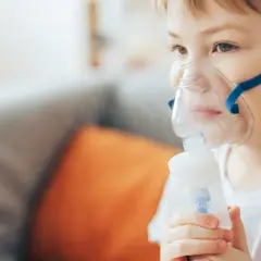 Chłopiec w masce nebulizatora wykonuje inhalację.