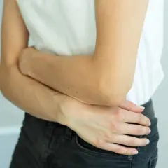 Kobieta trzymająca się za brzuch w białej koszulce i czarnych jeansach.