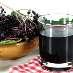 Szklanka ciemnego soku z czarnego bzu, idealnego dla dzieci, obok miski pełnej świeżych owoców kobylaku.