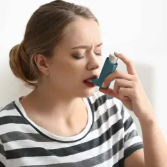 Kobieta z zamkniętymi oczami używa inhalatora na astmę.