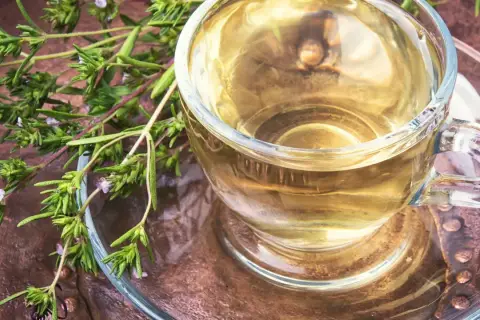 Aromatyczny napar z oregano, pełen dobroczynnych właściwości, w szklanej filiżance na rustykalnym tle.