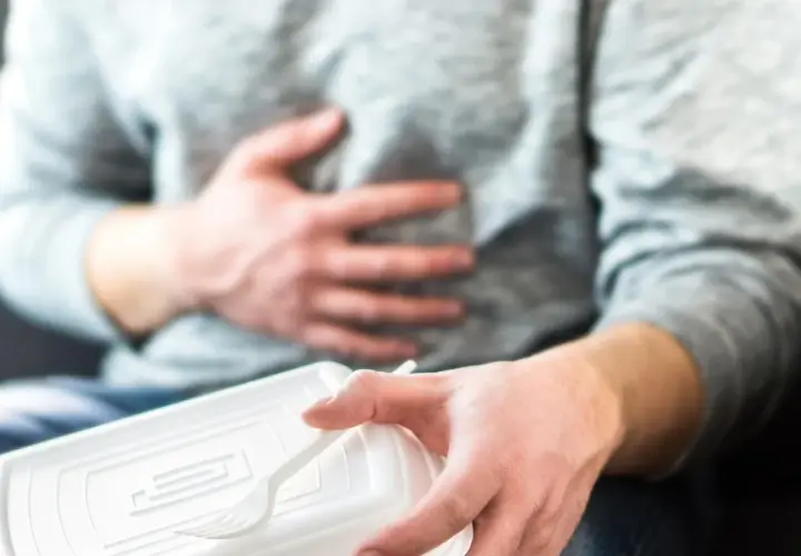Mężczyzna trzymający plastikowe pudełko z jedzeniem i trzymający się za brzuch.