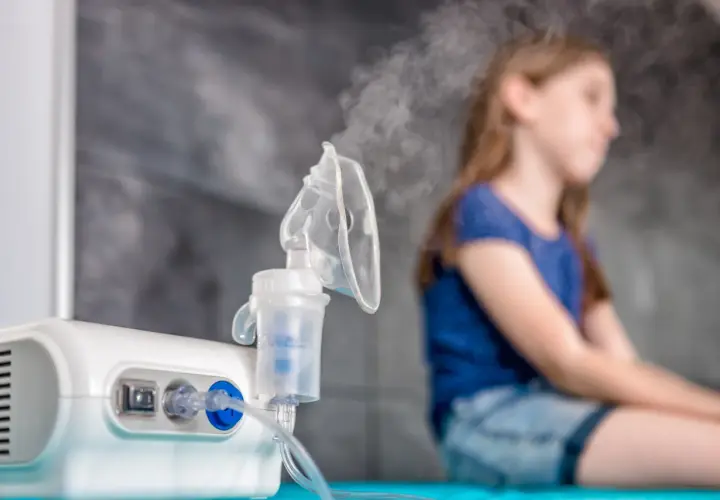 Inhalator z mgiełką i niewyraźna postać dziewczynki w tle.