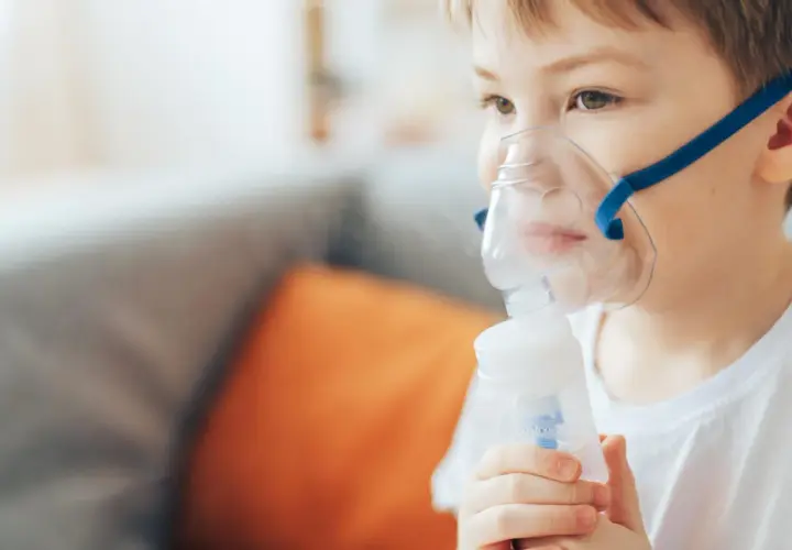 Chłopiec w masce nebulizatora wykonuje inhalację.