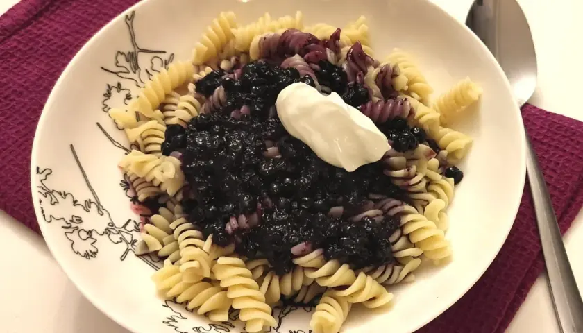 Fusilli z jagodami i kleksem śmietany na talerzu z czarnymi wzorami.