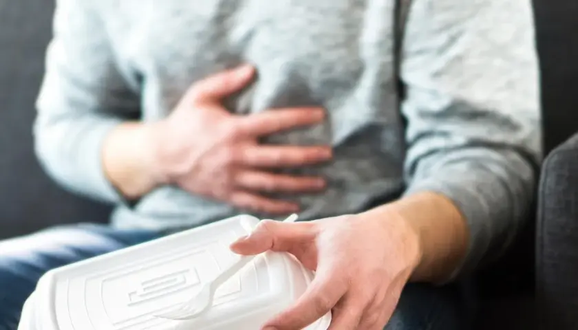 Mężczyzna trzymający plastikowe pudełko z jedzeniem i trzymający się za brzuch.