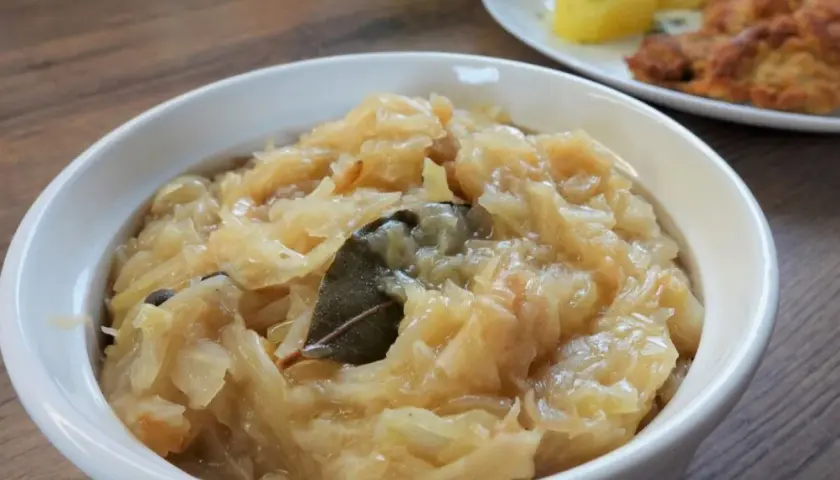 Pyszna kapusta kiszona zasmażana z liściem laurowym i zielem angielskim, podana w białej miseczce.