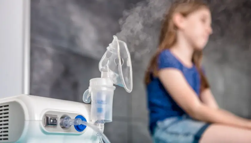 Inhalator z mgiełką i niewyraźna postać dziewczynki w tle.