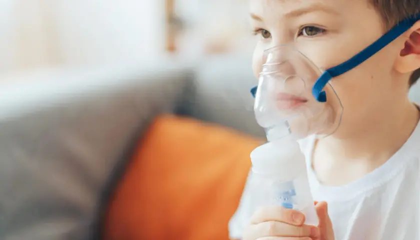 Chłopiec w masce nebulizatora wykonuje inhalację.