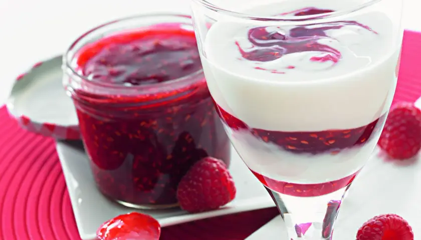 Sok z malin Thermomix w deserze jogurtowym. Słoiczek domowej konfitury malinowej obok.