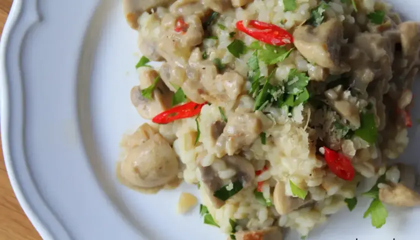 Kremowe risotto z pieczarkami, ozdobione natką pietruszki i ostrą papryczką. Idealne danie dla miłośników grzybów.