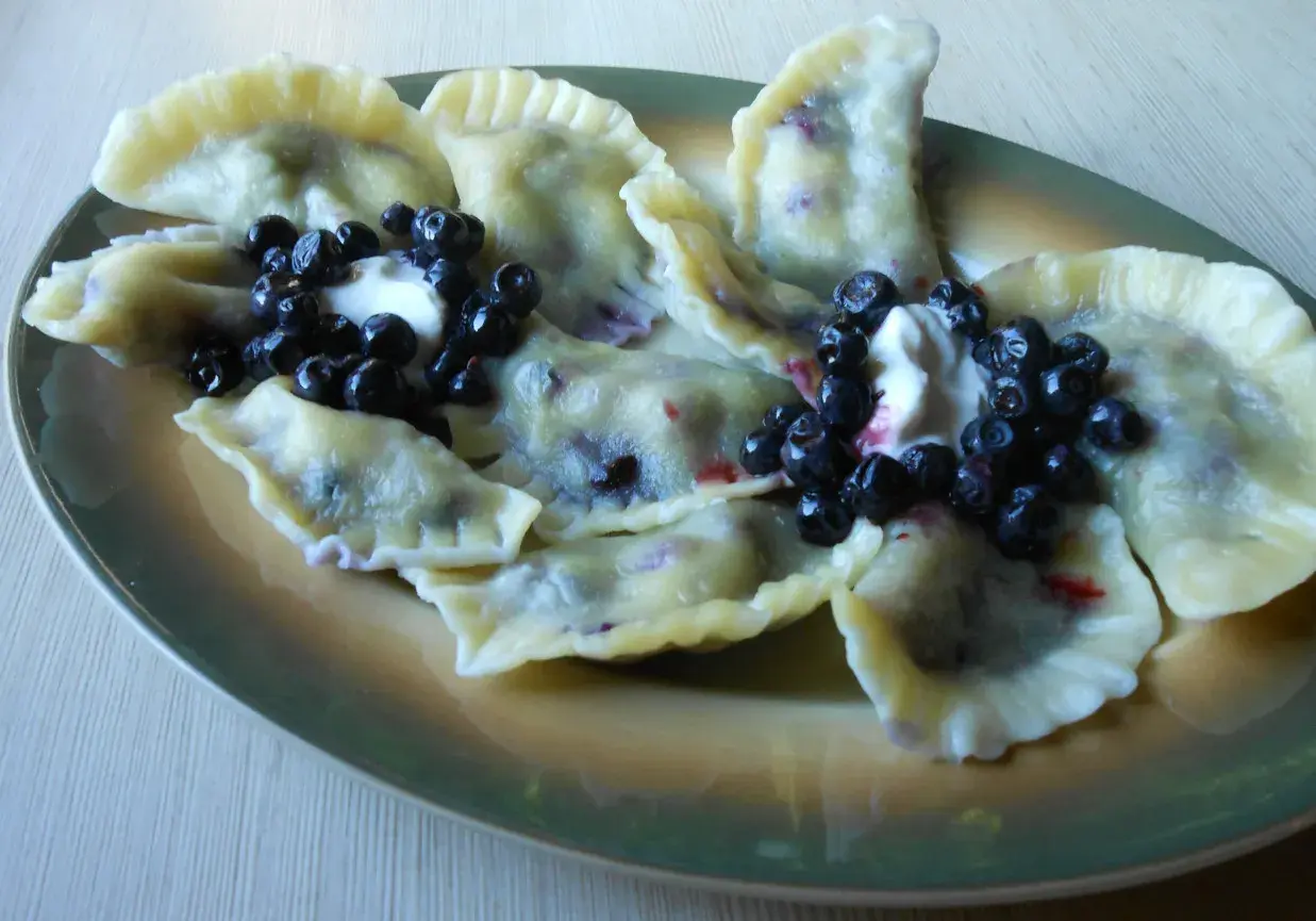 Pyszny przepis na pierogi z jagodami mrożonymi. Podane z bitą śmietaną i świeżymi jagodami.