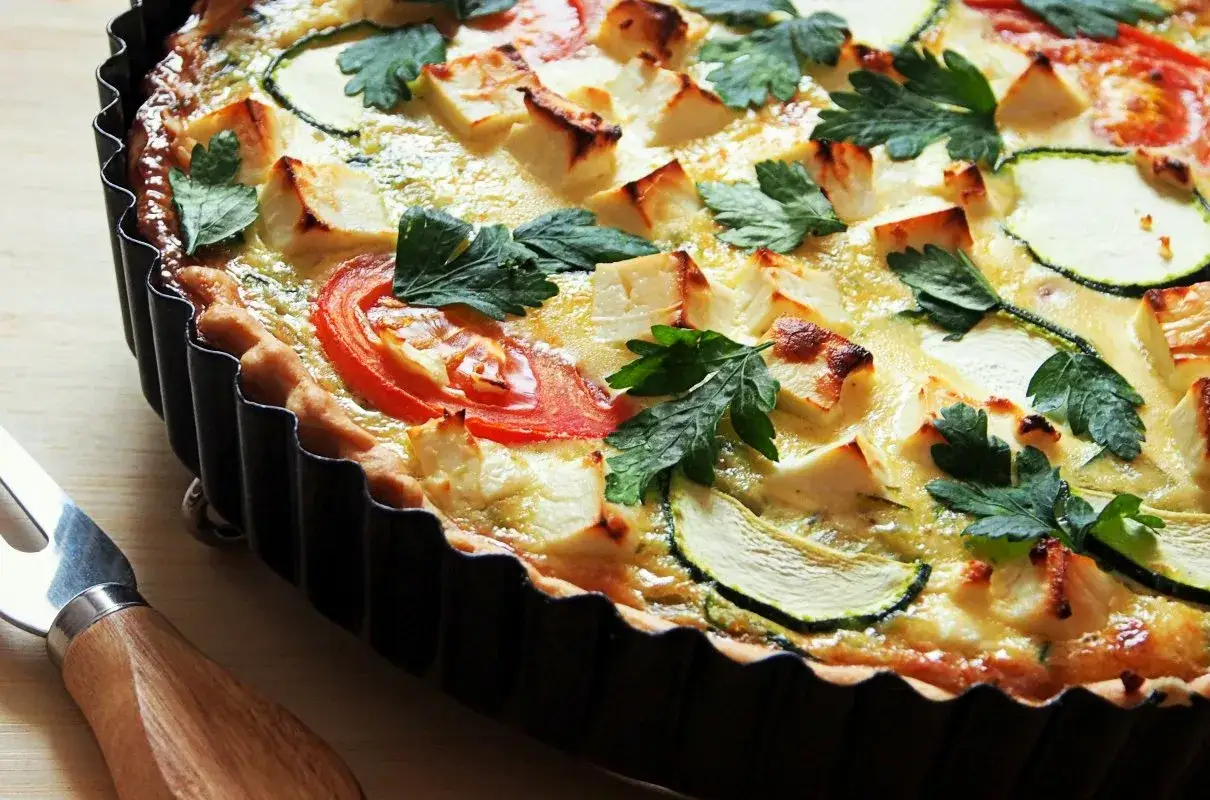 Pyszna tarta warzywna z cukinią, pomidorami i serem feta, udekorowana natką pietruszki. Idealna na lekki obiad.